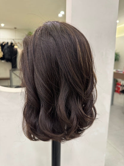 Dark brown hairpiece on a white surface with a blurred background